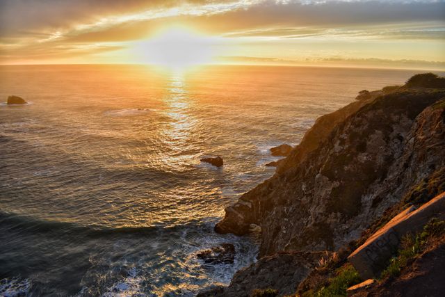 Beautiful golden sunset over the vast ocean with rocky cliffs in the foreground. Perfect for travel websites, inspirational quotes, nature blogs, and background images for presentations or screensavers. This peaceful and scenic view captures the tranquil essence of coastal landscapes.