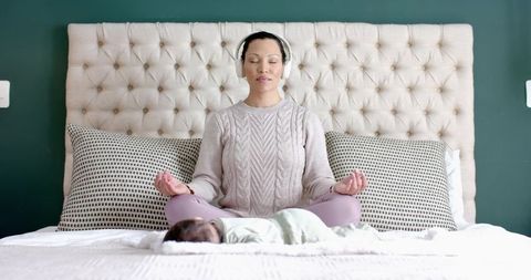 Asian mother meditating on bed with baby highlighting maternal serenity