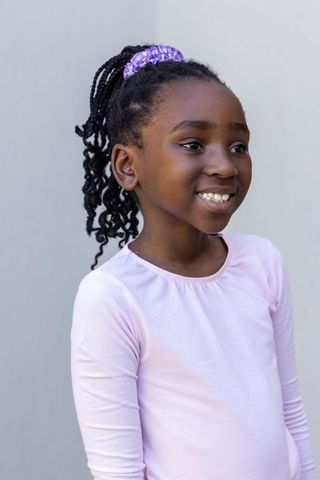 Smiling african girl wearing purple scrunchie and pink top posing against neutral gray