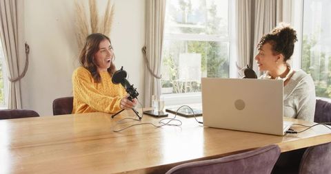Diverse cohosts recording intimate podcast at home table with laptop and tabletop mics