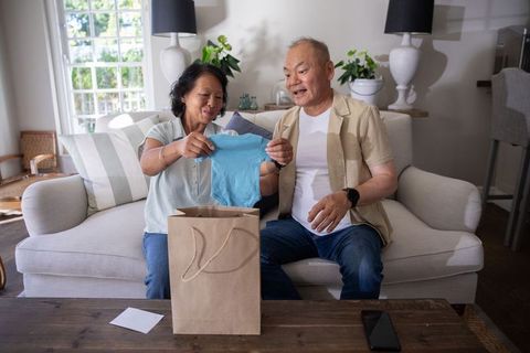 Senior asian couple holding blue baby onesie celebrating grandparent announcement joy