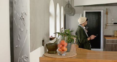 Indian man standing in modern rustic kitchen holding phone by wooden counter with oranges
