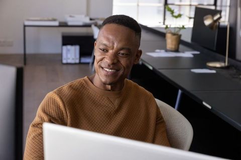 African american man working at minimalist office desk smiling at computer monitor
