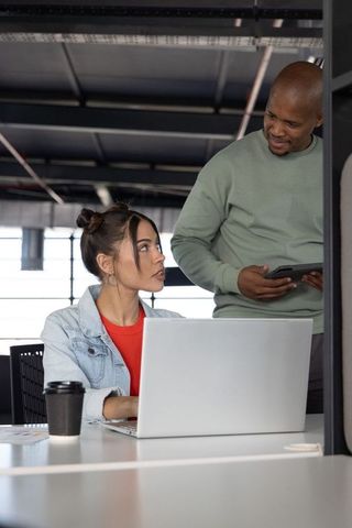 Diverse coworkers collaborating at desk using laptop and tablet in modern office