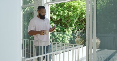 African American Man Holding Coffee Mug Checking Smartphone Outdoors