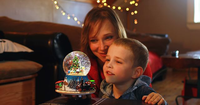 Mother and Son Gazing at Christmas Snow Globe with Lights in Background - Download Free Stock Images Pikwizard.com