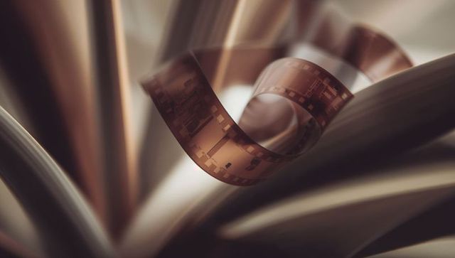 Curling 35mm film strip weaving through fanned book pages, vintage golden bokeh