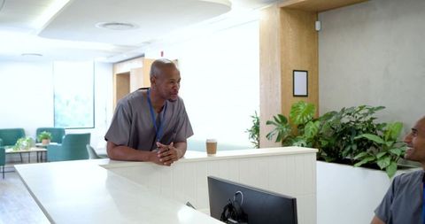 Medical staff collaborating at clinic reception desk in scrubs with plants and daylight