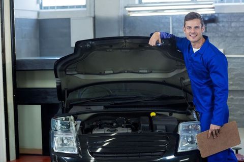 Male mechanic holding clipboard beside car in auto workshop