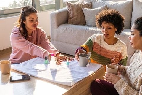 Multiracial friends having at-home manicure and coffee in cozy sunlit living room