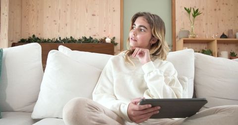 Woman Reflecting on Minimalist Living Room Sofa with Tablet