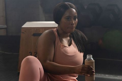 African american woman sitting on gym floor holding bottle during post-workout recovery