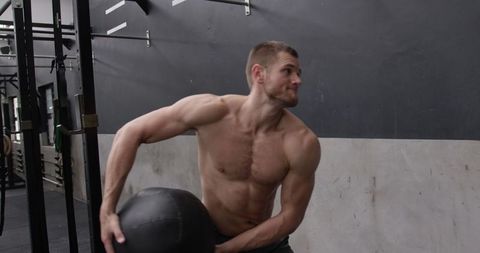 Muscular man throwing medicine ball at gym
