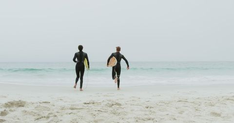 Adventurous Surfers Running on Sandy Beach with Surfboards