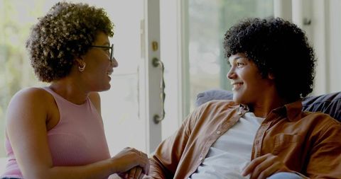 Sunlit living room couple sharing warm conversation and smiles on couch near patio door