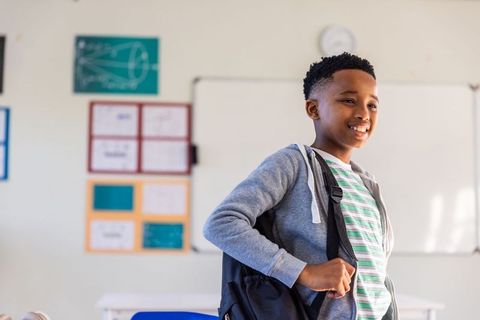 African american teen boy standing in sunlit classroom wearing backpack and hoodie