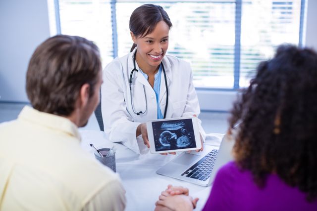 Doctor showing ultrasound scan to expectant couple in hospital. Ideal for use in healthcare, pregnancy, and family planning content. Can be used in articles, blogs, and advertisements related to prenatal care, medical consultations, and technology in healthcare.