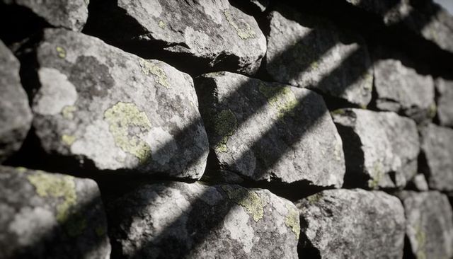 Weathered dry-stone wall with lichen patches and diagonal sunlight shadows, rustic closeup