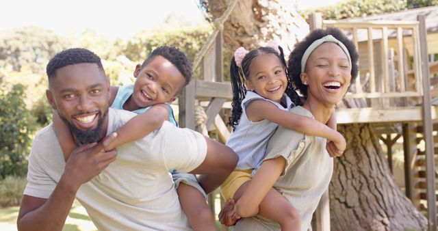 A joyful moment featuring a father and mother giving piggyback rides to their excited children, set in an outdoor garden with a treehouse in the background. Perfect for illustrating family togetherness, outdoor fun, and healthy living. Suitable for campaigns focused on family life, parenting tips, and recreational activities.