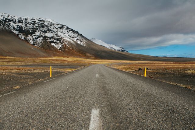 Empty road pointing towards majestic snow-capped mountains on a cloudy day. Ideal for themes of travel, adventure, and exploration. Perfect for nature-related projects, inspirational materials, or travel guides.
