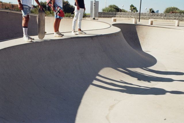 Two friends are standing at the edge of a skatepark holding skateboards and casting long shadows. This scene is perfect for illustrating youth culture, outdoor activities, and the skateboarding lifestyle. It can be used in marketing materials targeting young audiences, in sports and recreation magazines, or on social media to promote active lifestyles and community engagement.