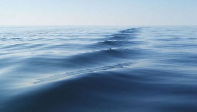 Calm ocean surface rippling toward horizon with linear wave ridge, tranquil blue seascape