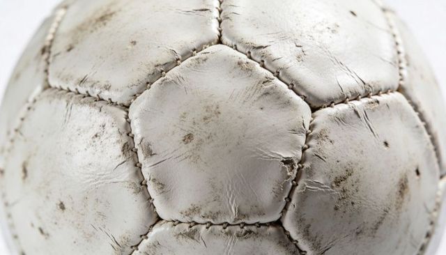 Worn white soccer ball close-up showing weathered leather, frayed stitching and scuff marks