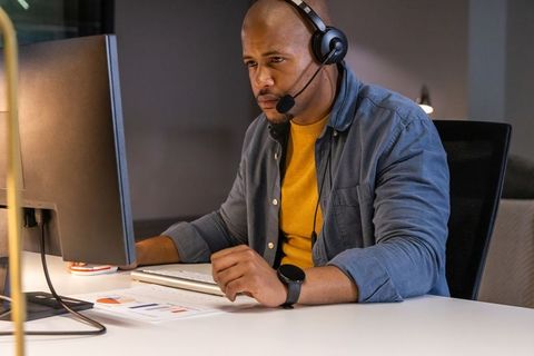 Focused african american it support specialist wearing headset working at desktop monitor