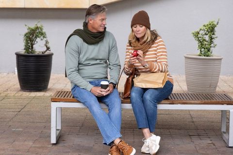 Senior couple enjoying coffee and apple on urban bench during autumn outing