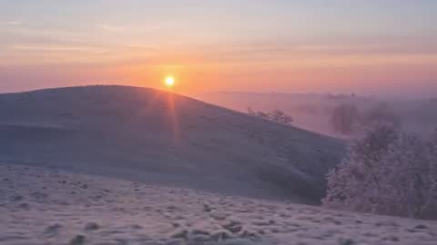 Sun rising over frost-covered rolling hills, pastel dawn mist and warm golden glow