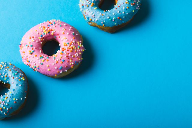 High angle view of donuts with colorful sprinkles on blue background. Perfect for illustrating themes of indulgence, sweet treats, and bright, fun designs. Ideal for use in food blogs, bakery menus, advertising campaigns, and social media promotions.