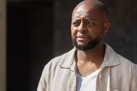 Squinting african man standing in sunlight wearing beige textured overshirt and white tee