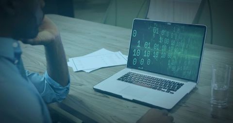Leaning professional reviewing binary code on laptop at conference table with papers and glass