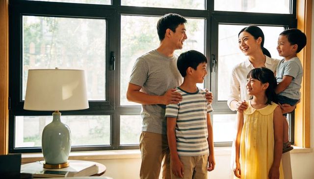 Smiling family sharing warm daylight moment by multi-pane black-framed window at home