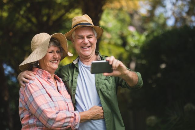 Happy senior couple taking selfie through mobile phone in yard
