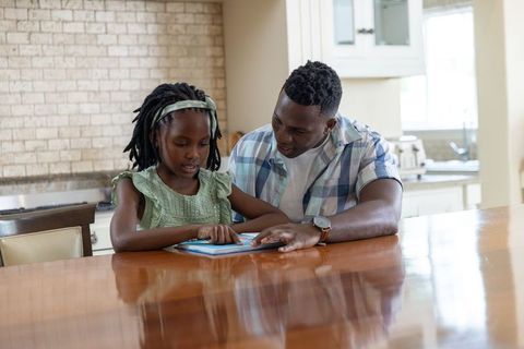 African american father helping daughter learn on tablet at bright kitchen table