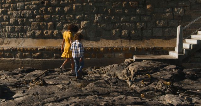 Happy biracial mother and son walking to steps holding hands on sunny rocky beach, copy space. Motherhood, childhood, togetherness, summer, vacations and free time, unaltered.