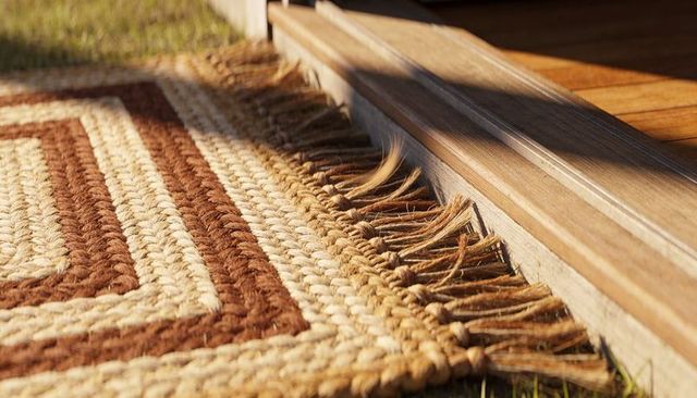 Sunlit braided jute rug at wooden threshold with tassels rustic porch entryway golden glow