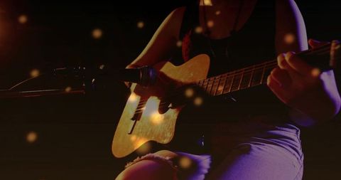 Teen musician playing acoustic guitar closeup with microphone and warm bokeh lights