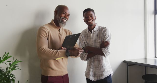 Two businessmen smiling and shaking hands in a modern office, symbolizing a successful partnership. Can be used for business, collaboration, teamwork, or professional relationship themes. Ideal for marketing materials, promotional content, or business websites.
