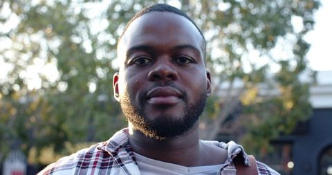 African American man standing outdoors looking confident wearing plaid overshirt in warm sunlight