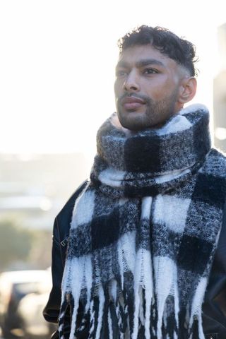 Backlit urban portrait man wearing oversized black white plaid scarf for winter fashion