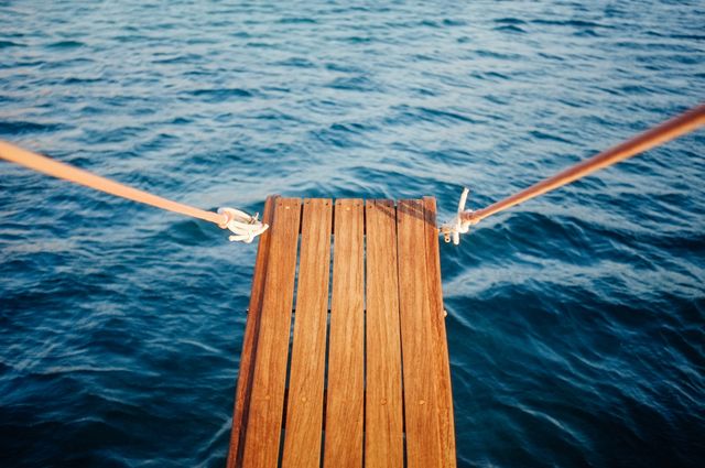 Wooden dock extends over calm blue ocean water. Ideal for conveying vacation, relaxation, serenity, and exploration. Great use in travel brochures, outdoor adventure ads, or nature-themed articles.