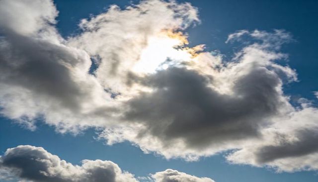 Dramatic cumulus cloud hiding sun with iridescent rim over deep blue sky, moody skyscape