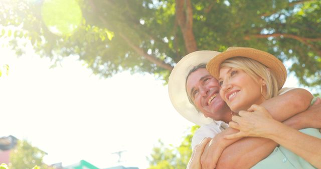 Senior couple enjoying time outside, hugging in a sunlit park. Bright, happy, and tranquil, evoking feelings of love and companionship. Can be used for topics on retirement, healthy aging, love in golden years, outdoor activities, and family-oriented campaigns.