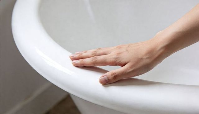 Resting hand touching glossy porcelain tub rim showing ceramic bath edge and floor tiles