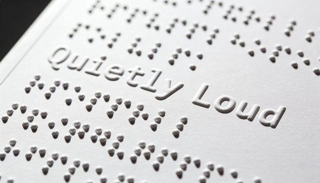 Embossed braille and raised text quietly loud on white textured cardstock close-up