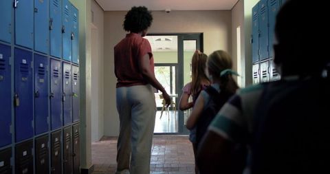 African american teacher leading elementary students through locker corridor to classroom