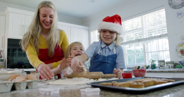Mother and her two children are happily baking cookies together in a bright and cozy kitchen. The little boy wears a Santa hat, adding a festive touch. The scene shows flour, eggs, and dough on the counter, capturing the joy of holiday preparations. This image is perfect for advertisements, holiday greeting cards, family activity promotions, and seasonal blogs.