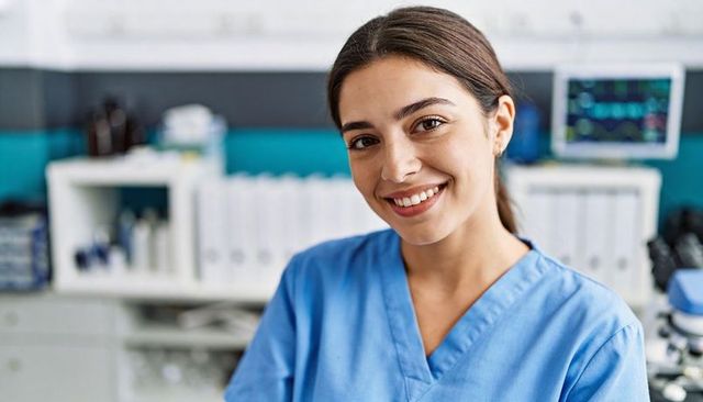 Smiling nurse wearing blue scrubs delivering compassionate care at clinic workstation